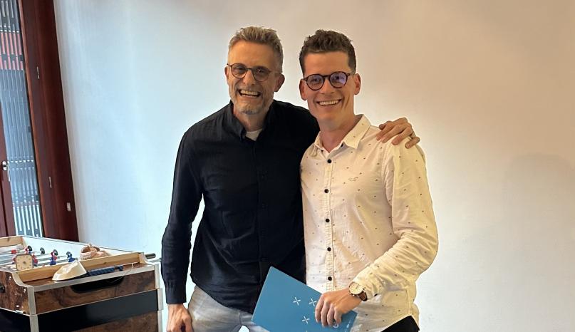 Zwei M&auml;nner auf dem Bild. Einer davon h&auml;lt eine Mappe in der Hand.