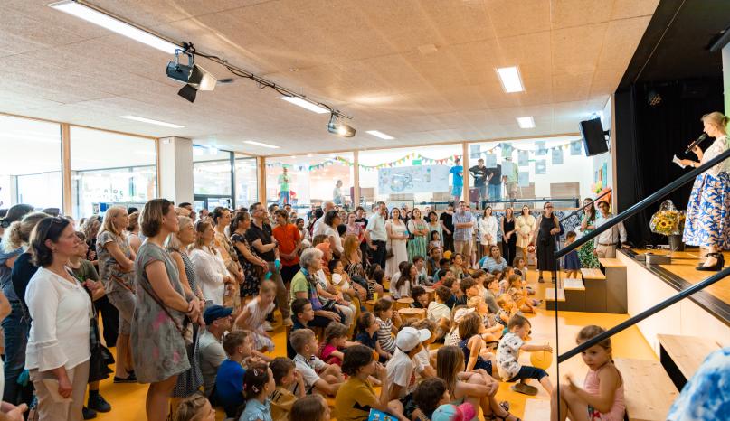 Kinder und Eltern in der Aula stehen und sitzen am Boden